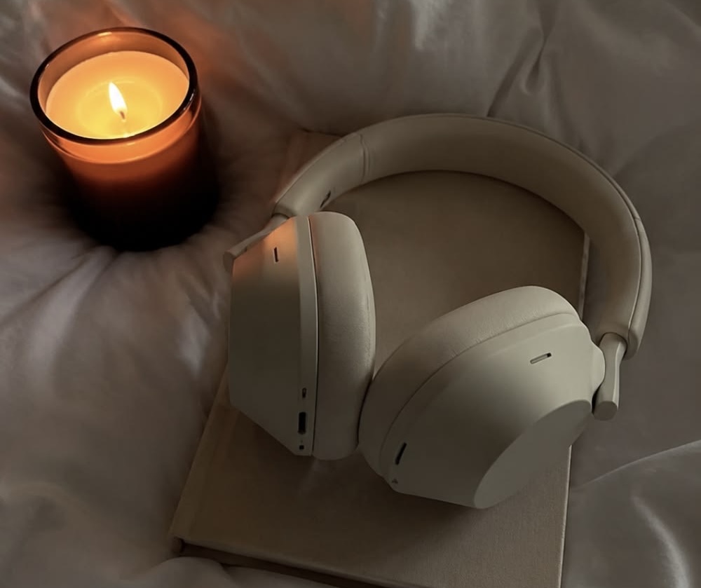 Fones de ouvido sobre um livro ao lado de uma vela acesa